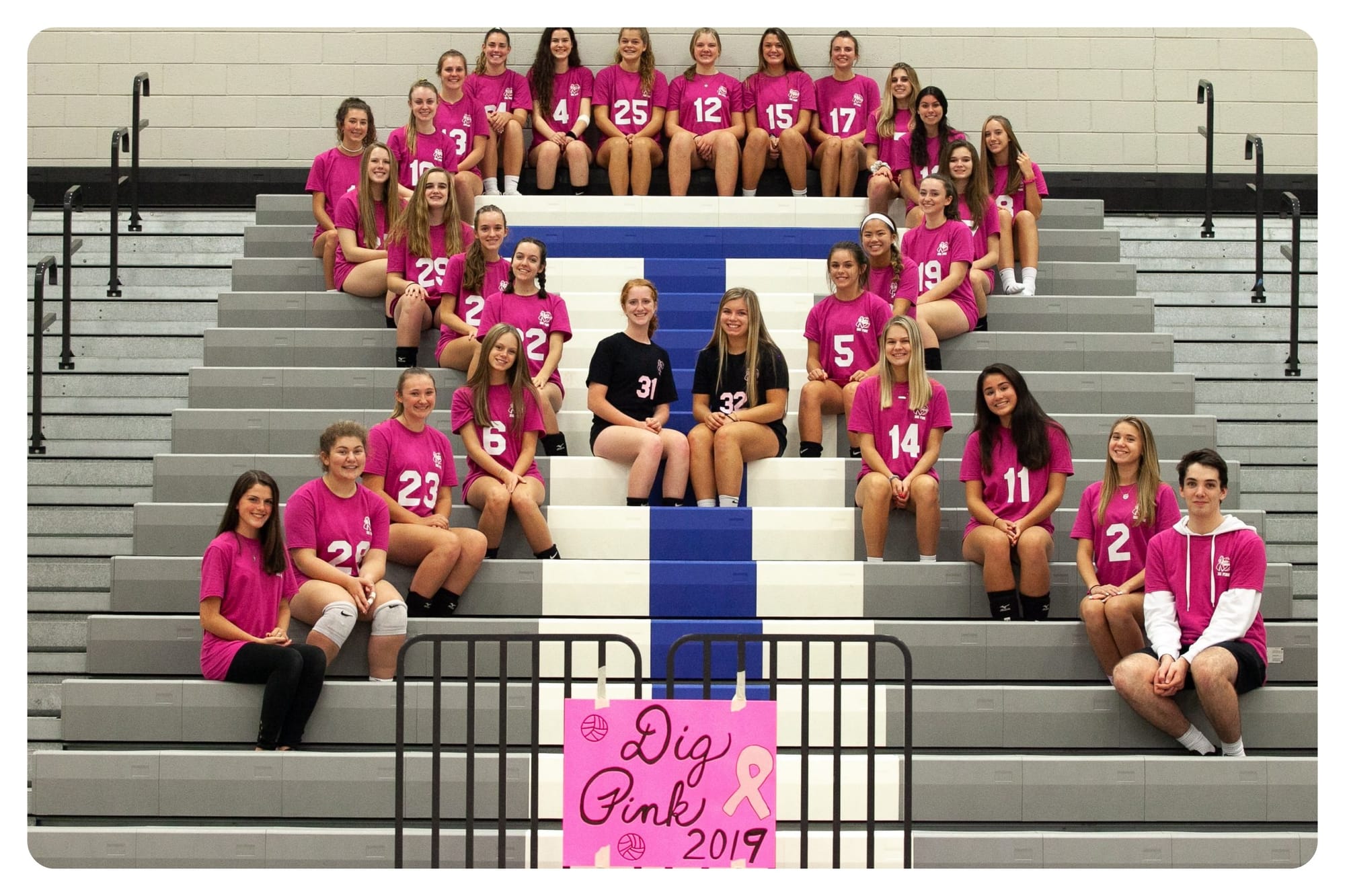 Team members sit on the school bleachers in a breast cancer ribbon formation.